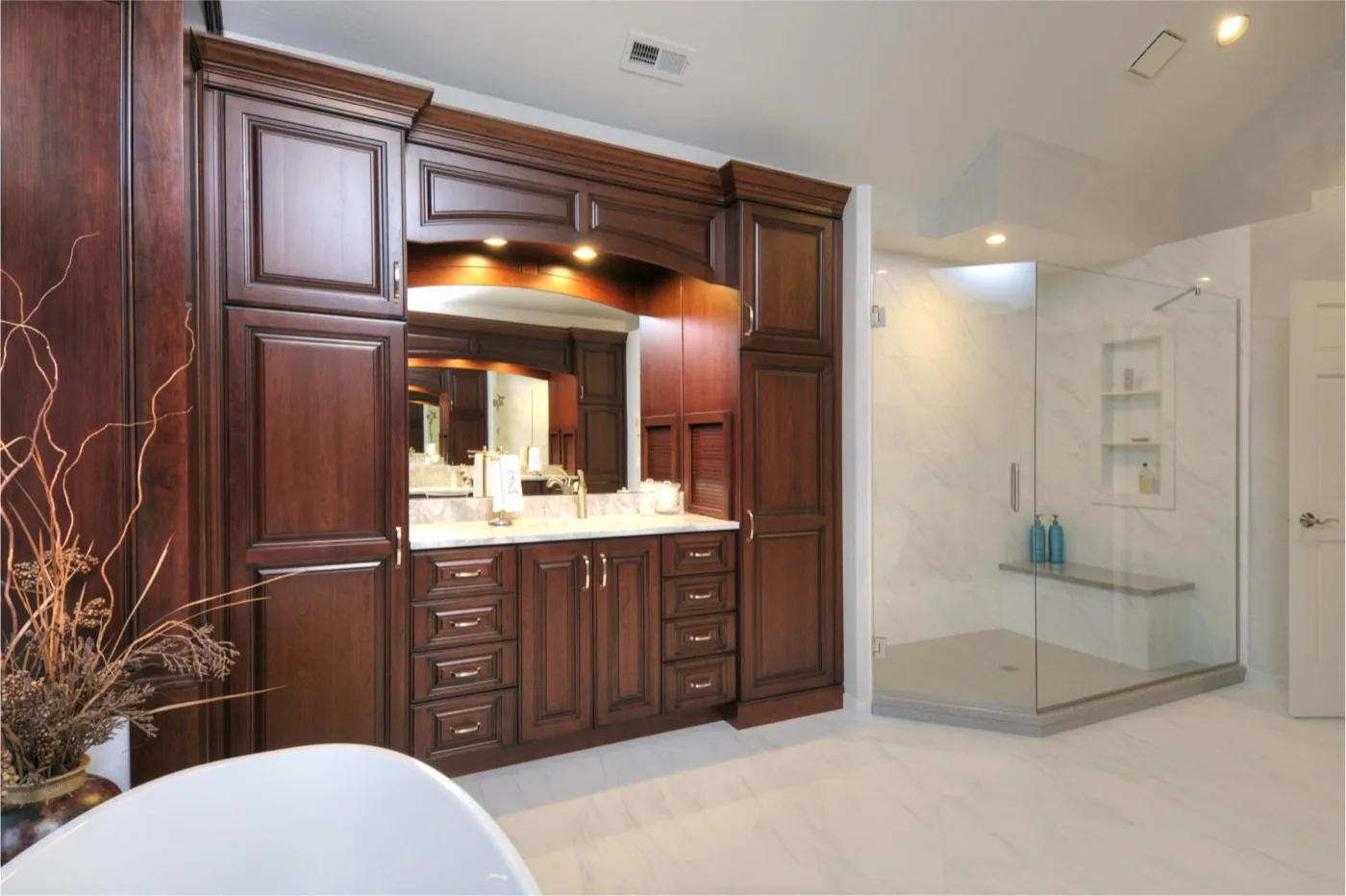 A cherry-finished dressing area and vanity next to a glass shower