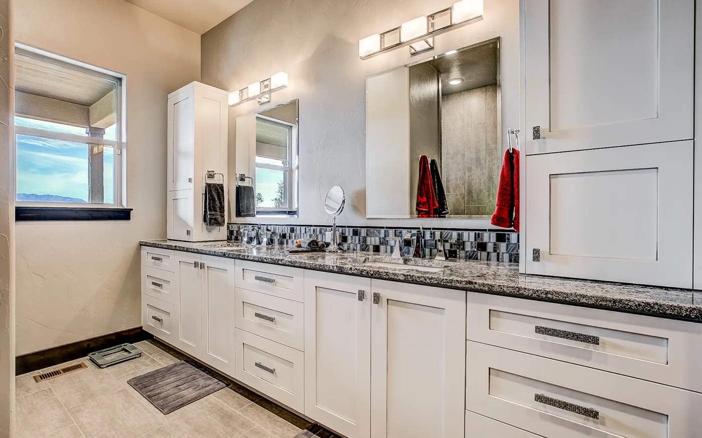 A finished bath with painted cabinetry, a long stone counter and twin mirrors