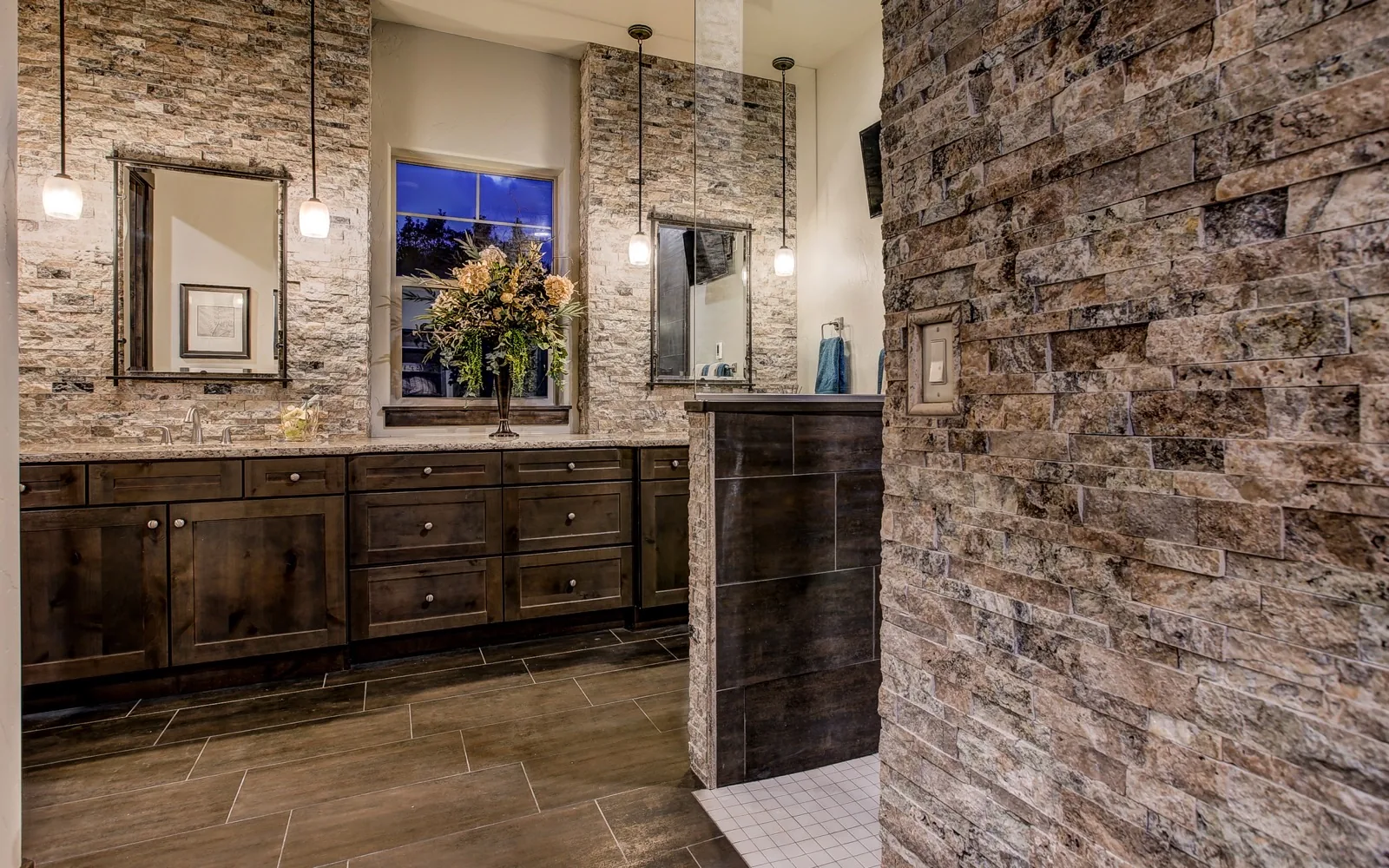 A bath with a stacked stone wall and a stained wood vanity