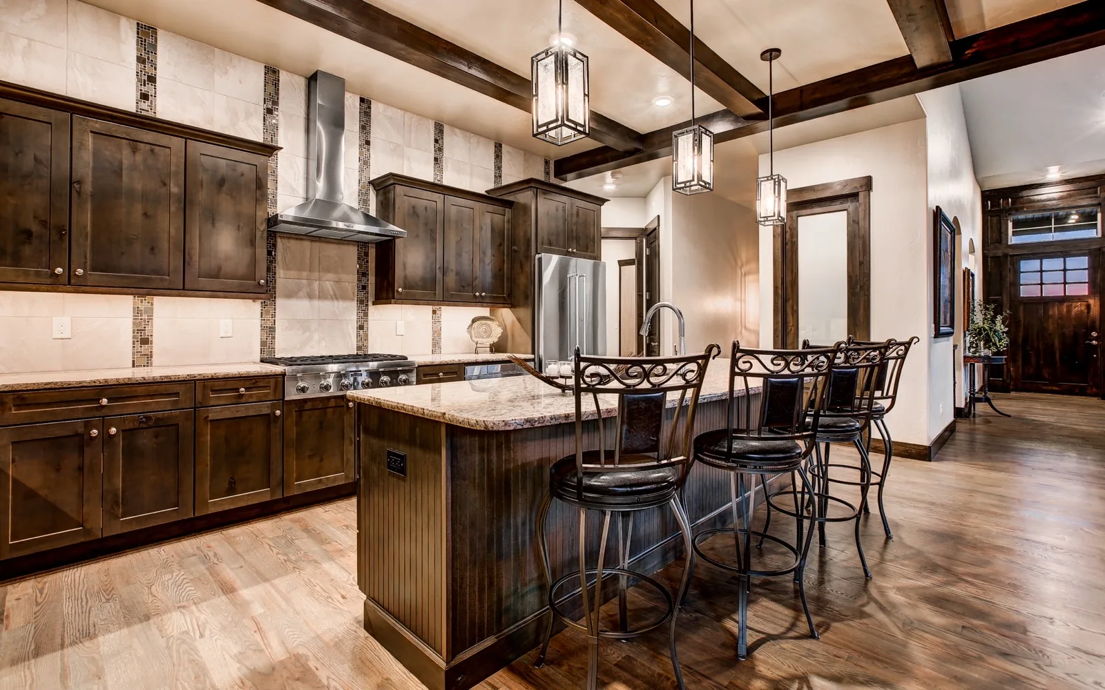 A stained wood kitchen with exposed beams, a hood and an island with seating