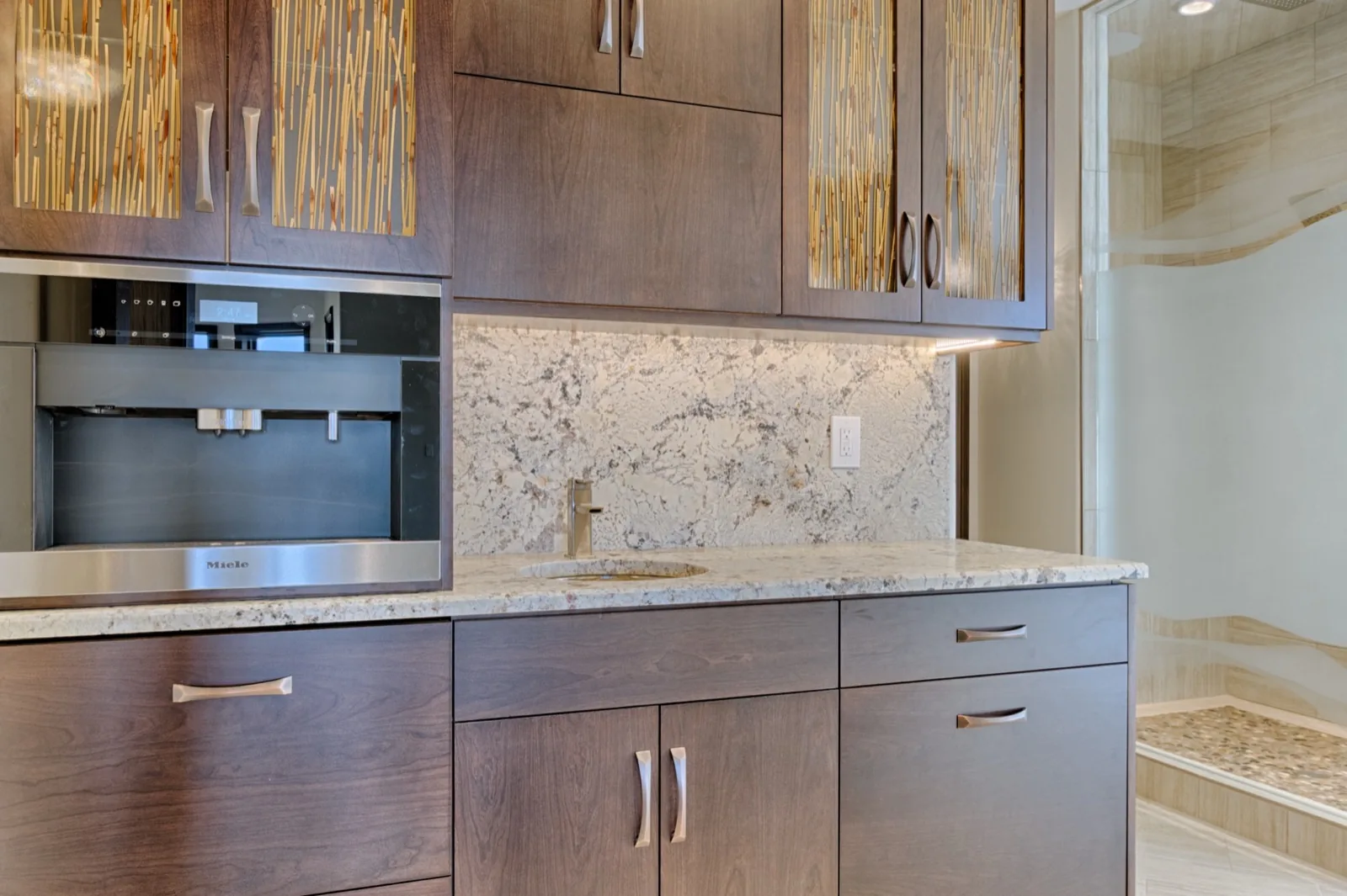 A beverage station with a built-in coffee machine and glass upper doors